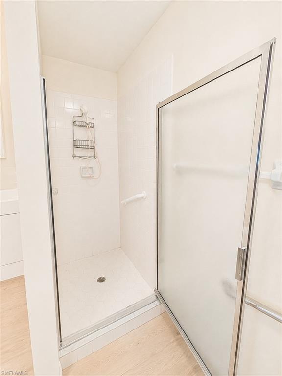 Spacious shower enclosure featuring white subway tile surround, clear glass shower door with metal framing, and a contrasting light wood-finish flooring outside