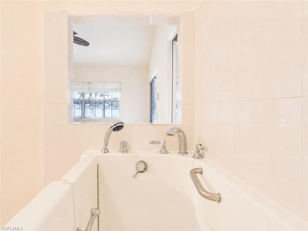 White tiled shower surround featuring a built-in tub with chrome fixtures, a handheld showerhead, and an integrated grab bar