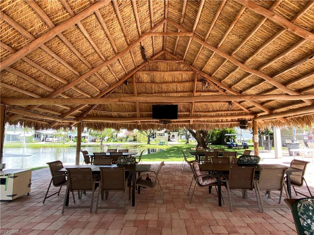 Expansive covered patio featuring a large thatch roof structure with exposed wood beams, a paver stone patio, and a tranquil water feature