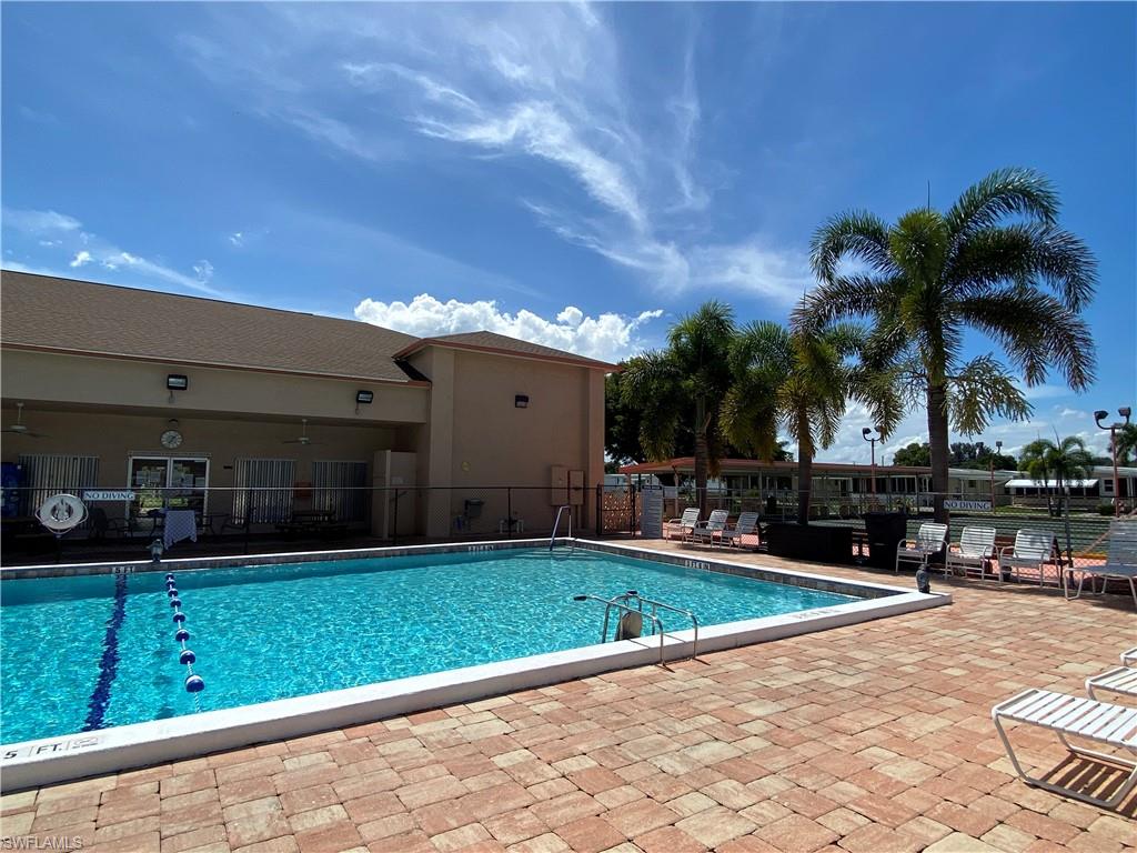 Expansive outdoor swimming pool featuring a paver stone deck, surrounding lounge chairs, and mature palm trees