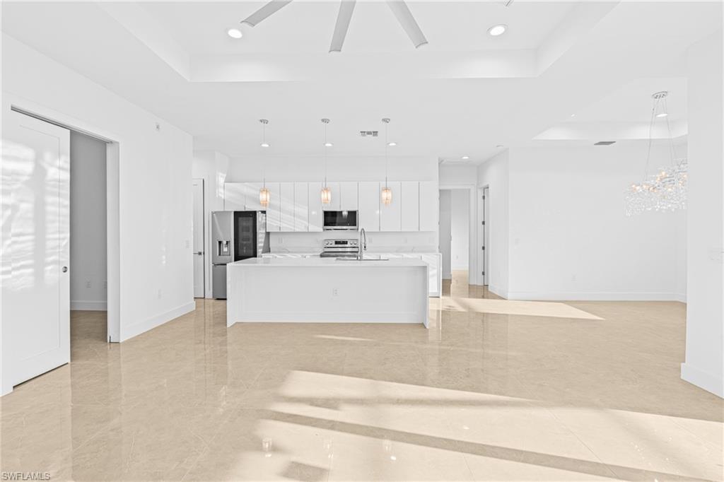 Kitchen featuring open floor plan, a kitchen island with sink, a tray ceiling, white cabinetry, and recessed lighting