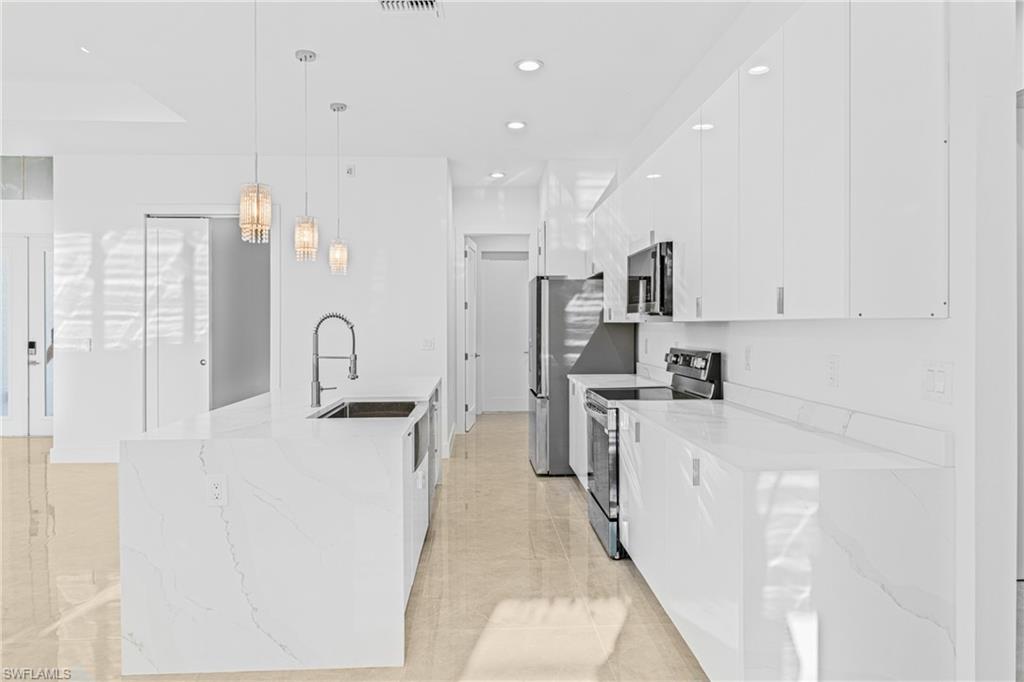 Kitchen featuring stainless steel appliances, decorative light fixtures, light stone countertops, white cabinetry, and light tile patterned floors