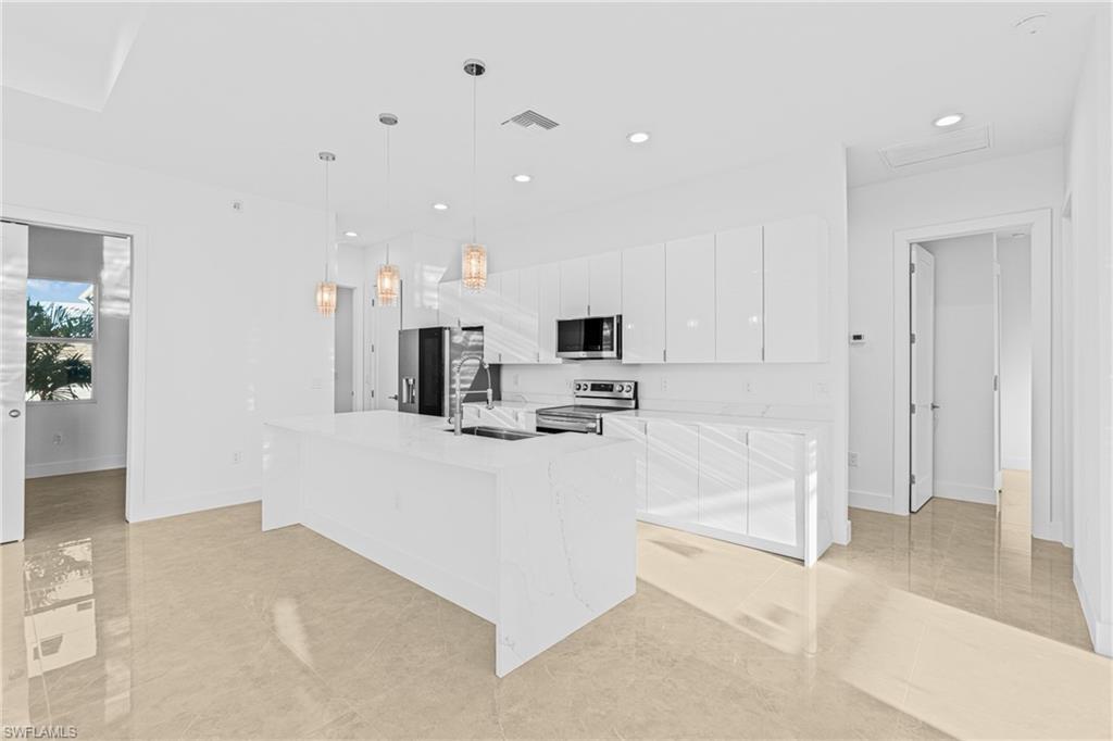 Kitchen with white cabinetry, pendant lighting, a center island with sink, appliances with stainless steel finishes, and light tile patterned flooring