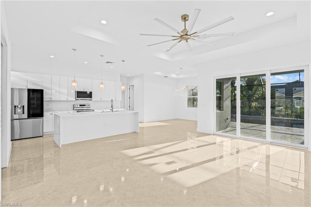 Unfurnished living room featuring a tray ceiling, recessed lighting, a chandelier, ceiling fan, and light marble finish floors