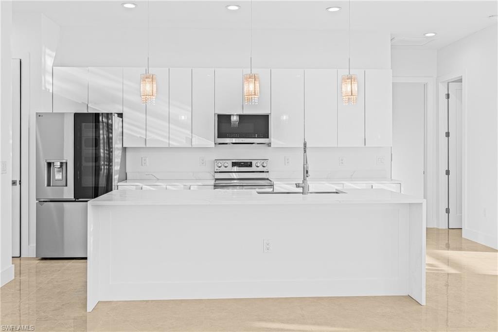 Kitchen featuring light stone countertops, stainless steel appliances, pendant lighting, white cabinets, and recessed lighting