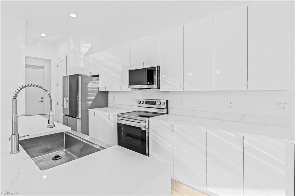 Kitchen with modern cabinets, stainless steel appliances, white cabinetry, light stone counters, and recessed lighting