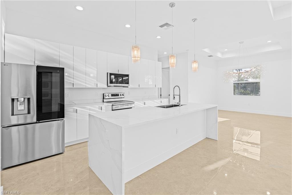 Kitchen featuring appliances with stainless steel finishes, pendant lighting, white cabinetry, light stone countertops, and recessed lighting