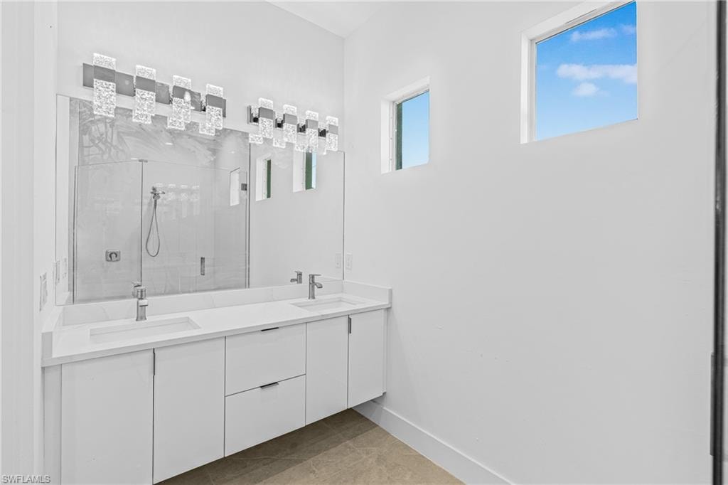 Full bathroom with double vanity, a marble finish shower, and light tile patterned floors