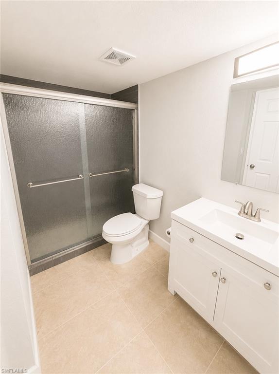 Bathroom featuring a glass-enclosed shower, white vanity with integrated sink, contemporary vanity lighting, mirror, and neutral-toned floor tiling