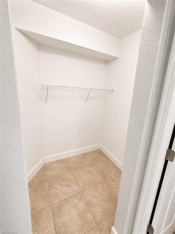 Interior closet featuring light-toned tile flooring, white baseboards, a built-in upper shelf, and a wire rack system