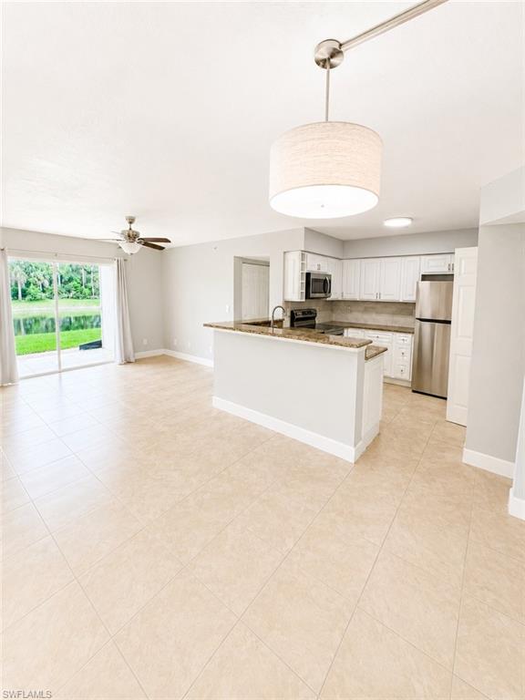 Open-concept living area with large format tile flooring, a kitchen island with stone countertops, white shaker cabinetry, stainless steel appliances, and a sliding glass door opening to outdoor space