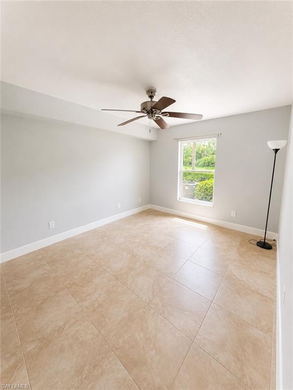 Spacious room featuring neutral wall tones, large format tile flooring, a window providing natural light, and a ceiling fan with integrated lighting