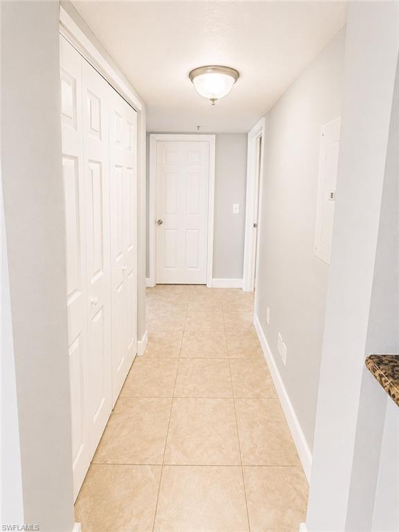 Hallway featuring neutral wall paint, tiled flooring, white baseboards, and a semi-flush mount ceiling light