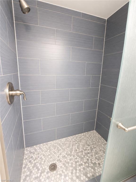 Walk-in shower featuring elongated rectangular wall tiles, hexagonal mosaic floor tiles, a brushed nickel showerhead, and a frosted glass shower door with a brushed nickel handle