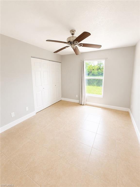 Room featuring large format beige tile flooring, a window with exterior views, and a ceiling fan with brushed nickel hardware