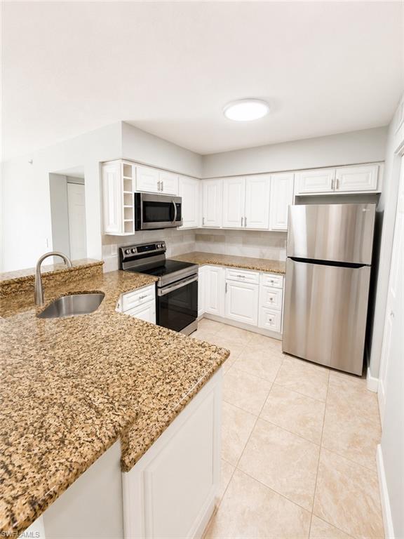 Kitchen featuring white cabinetry, stainless steel appliances, speckled stone countertops, and a tiled backsplash