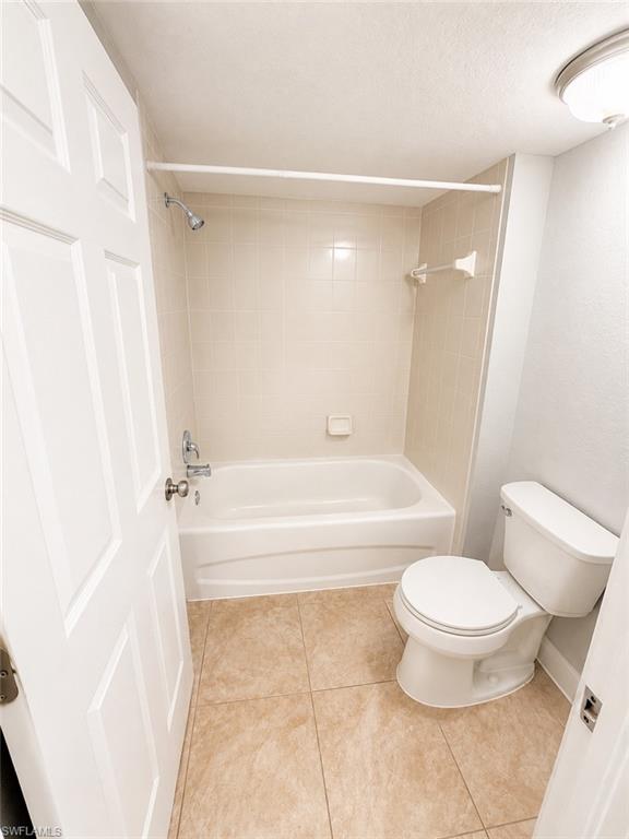 Bathroom featuring a white tub and shower combination with chrome fixtures, light-toned wall tiling, and a white toilet