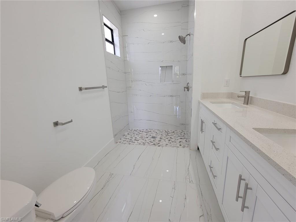 Bathroom featuring tile patterned floors, tiled shower, double vanity, and toilet