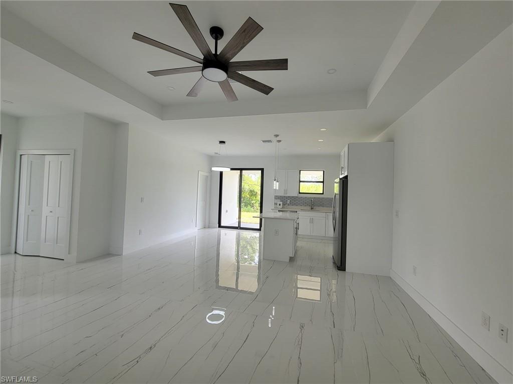Tiled empty room featuring ceiling fan and a raised ceiling
