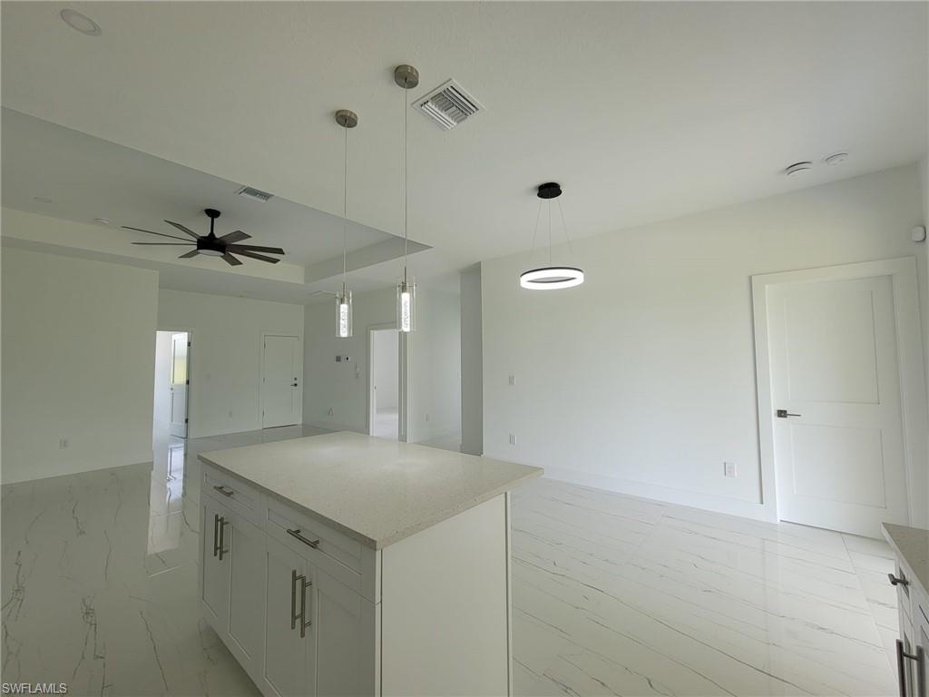 Kitchen with white cabinetry, a center island, ceiling fan, hanging light fixtures, and a raised ceiling