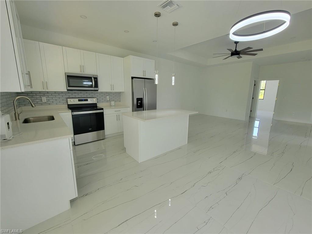 Kitchen featuring stainless steel appliances, white cabinets, a kitchen island, light tile patterned flooring, and ceiling fan