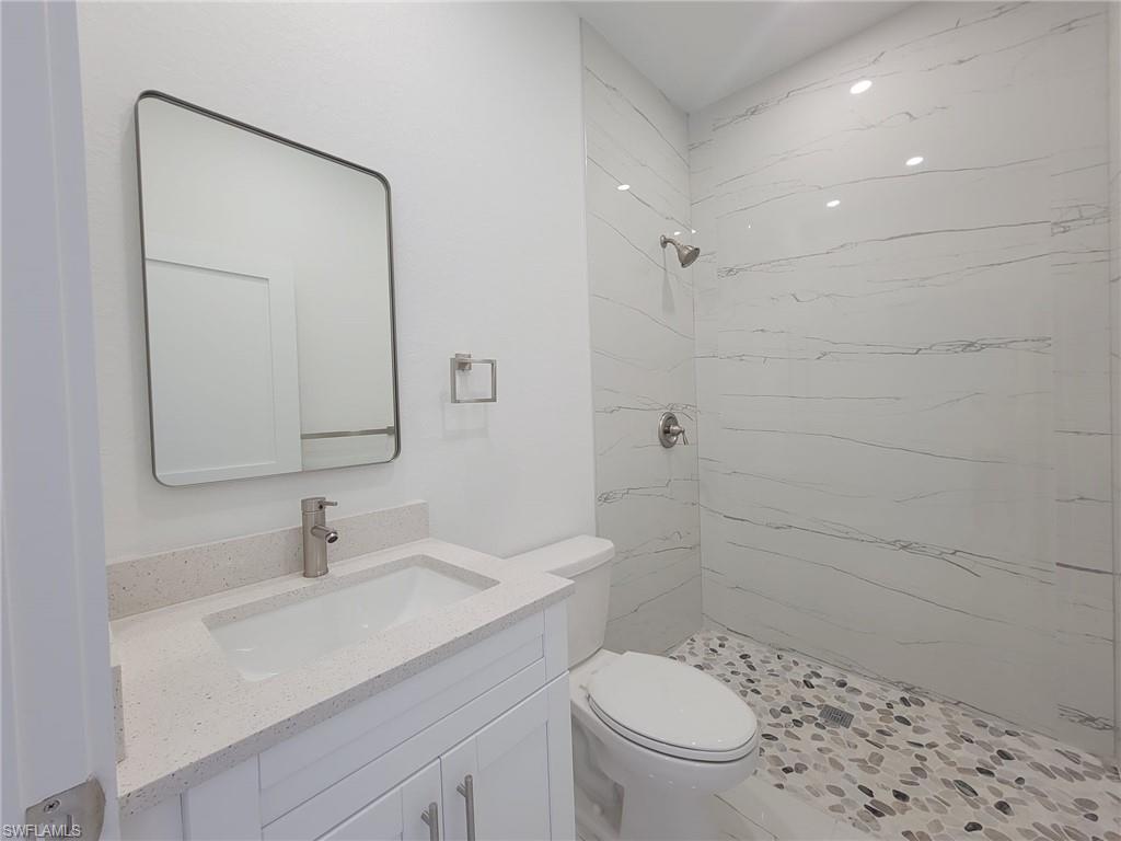 Bathroom featuring vanity, a tile shower, and toilet