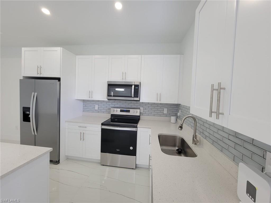 Kitchen featuring white cabinetry, stainless steel appliances, decorative backsplash, sink, and light stone countertops