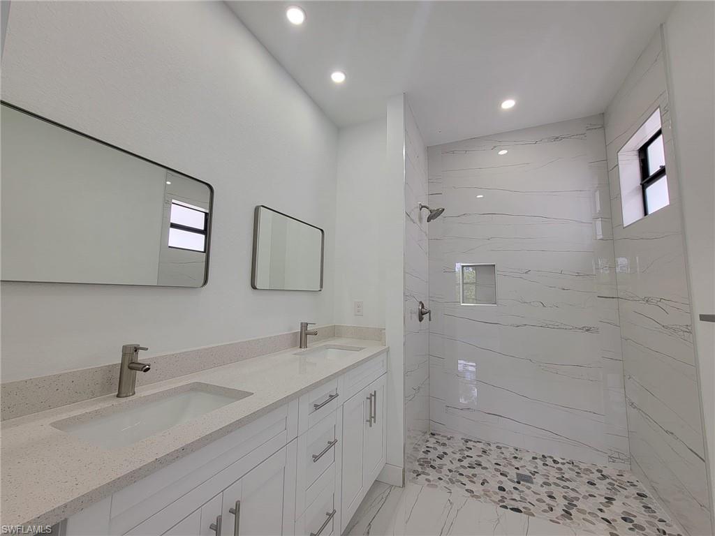 Bathroom featuring dual vanity, a tile shower, a healthy amount of sunlight, and tile patterned flooring