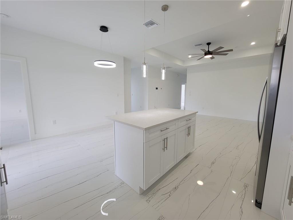 Kitchen with decorative light fixtures, stainless steel refrigerator, white cabinets, and a kitchen island