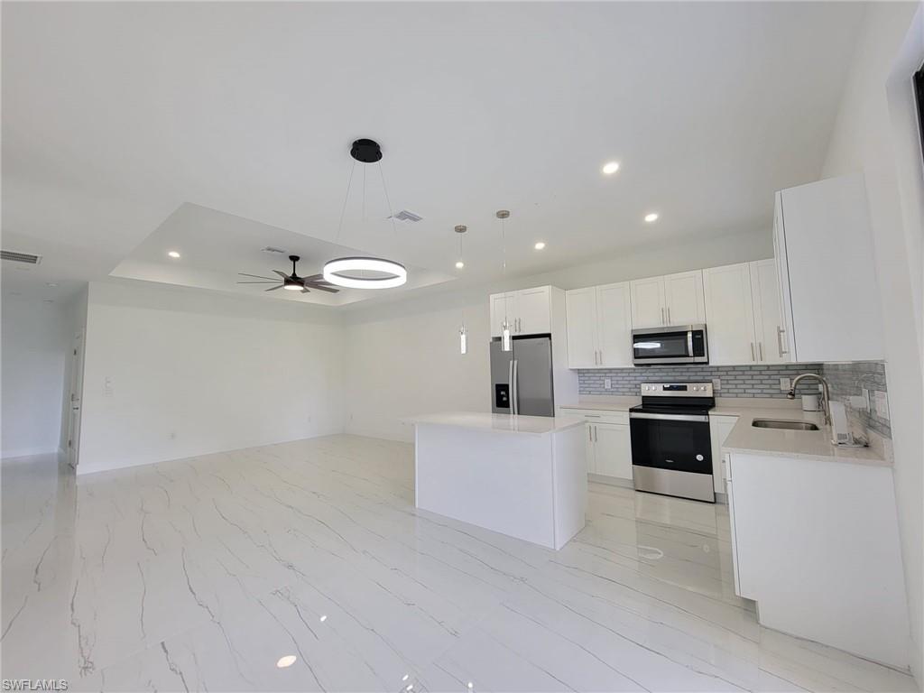Kitchen with a center island, ceiling fan, appliances with stainless steel finishes, decorative backsplash, and sink