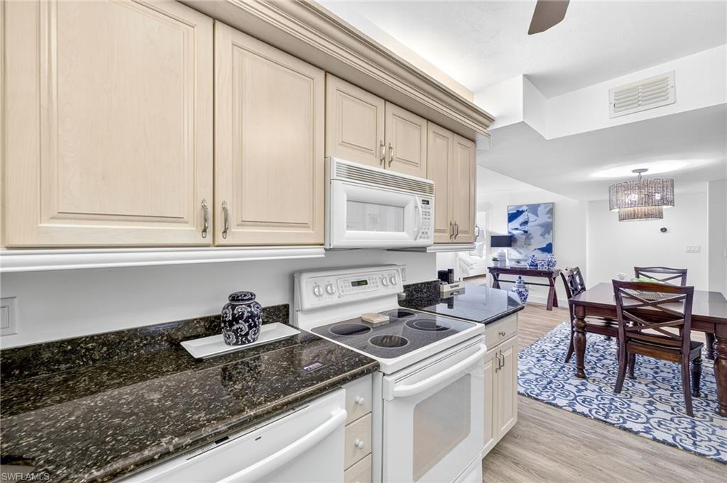Kitchen featuring white appliances, light wood-style floors, a chandelier, dark stone counters, and a ceiling fan