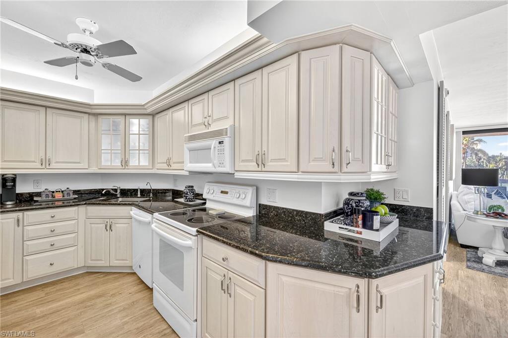 Kitchen featuring white appliances, light wood-type flooring, a ceiling fan, and dark stone countertops