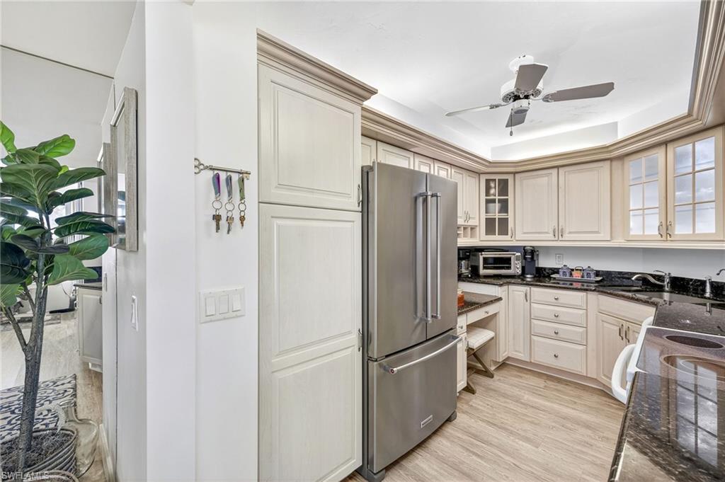Kitchen with high quality fridge, light wood-style flooring, dark stone counters, glass insert cabinets, and ceiling fan