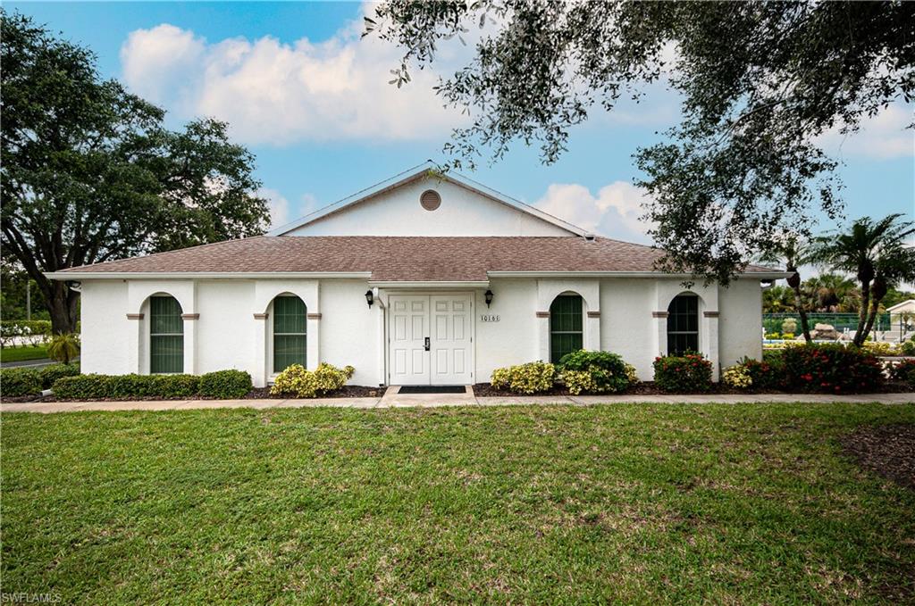 White stucco exterior with arched window details, a double entry door, mature landscaping, and a pitched shingle roof