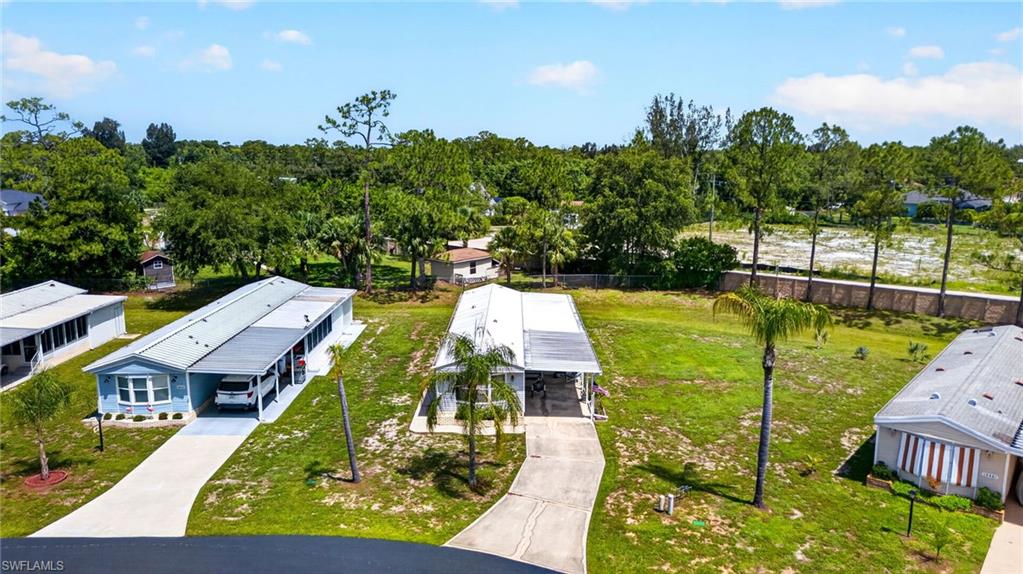 Paved driveway leading to a covered carport, surrounded by a grassy lawn and mature trees
