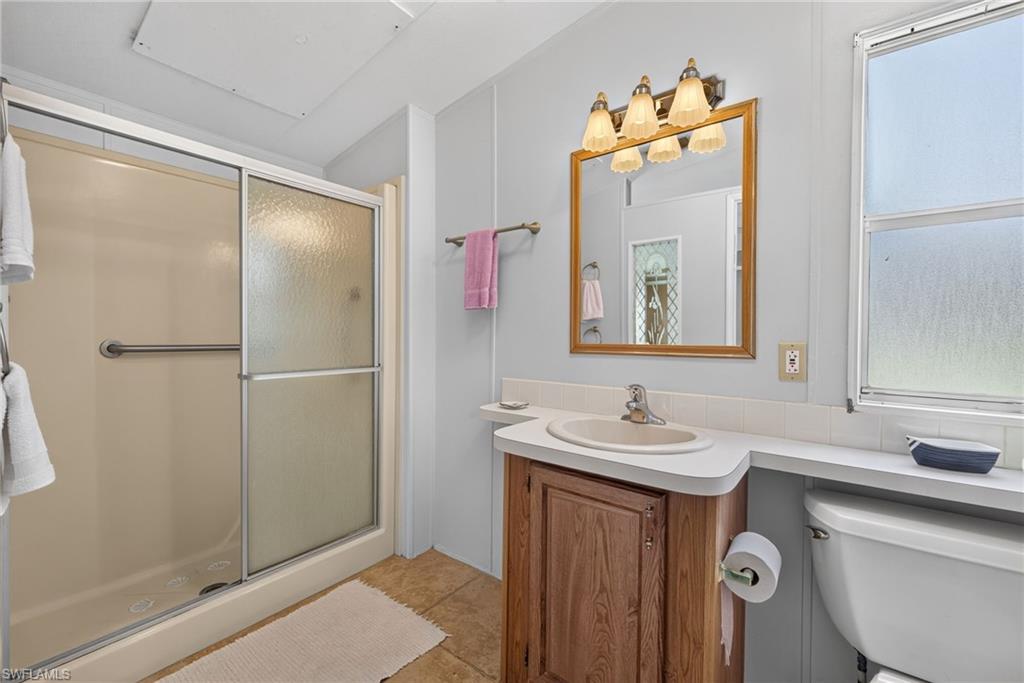 Full bath featuring a walk-in shower with sliding frosted glass doors, a single vanity with wood-finish cabinetry, a framed mirror, and a window providing natural light