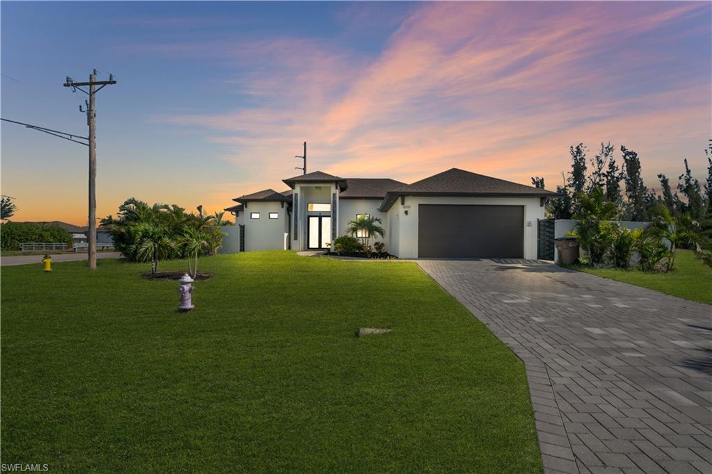 Modern stucco exterior with dark trim, dual garage doors, and a paver driveway