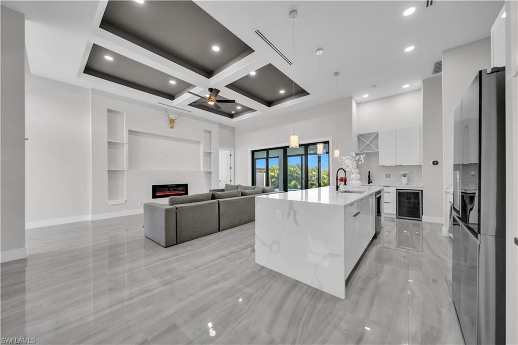 Open-concept living space featuring a tray ceiling with recessed lighting, an electric fireplace, a kitchen island with a waterfall edge, and sliding glass doors