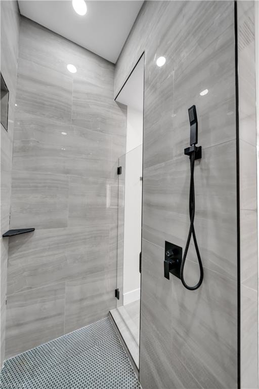 Shower with full-height light gray tile walls, mosaic tile flooring, a matte black shower system, and a black corner shelf