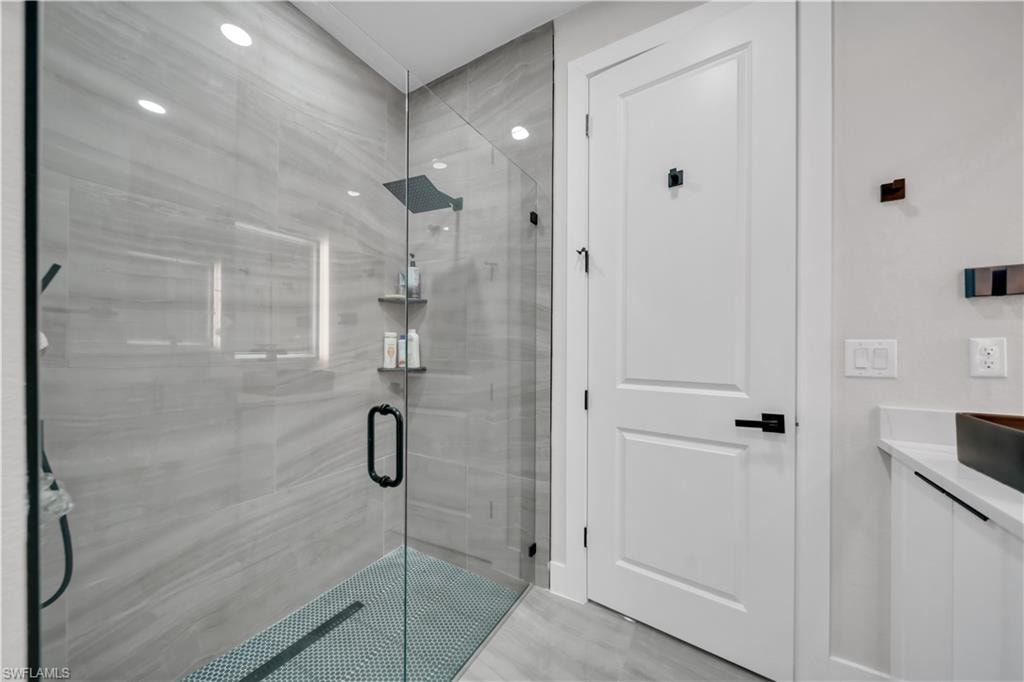 Glass-enclosed shower with gray tile walls, mosaic tile floor, and a matte black showerhead