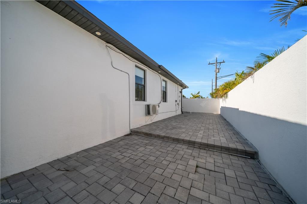 Paver patio with an elevated section, surrounded by white stucco walls, featuring a window and exterior lighting