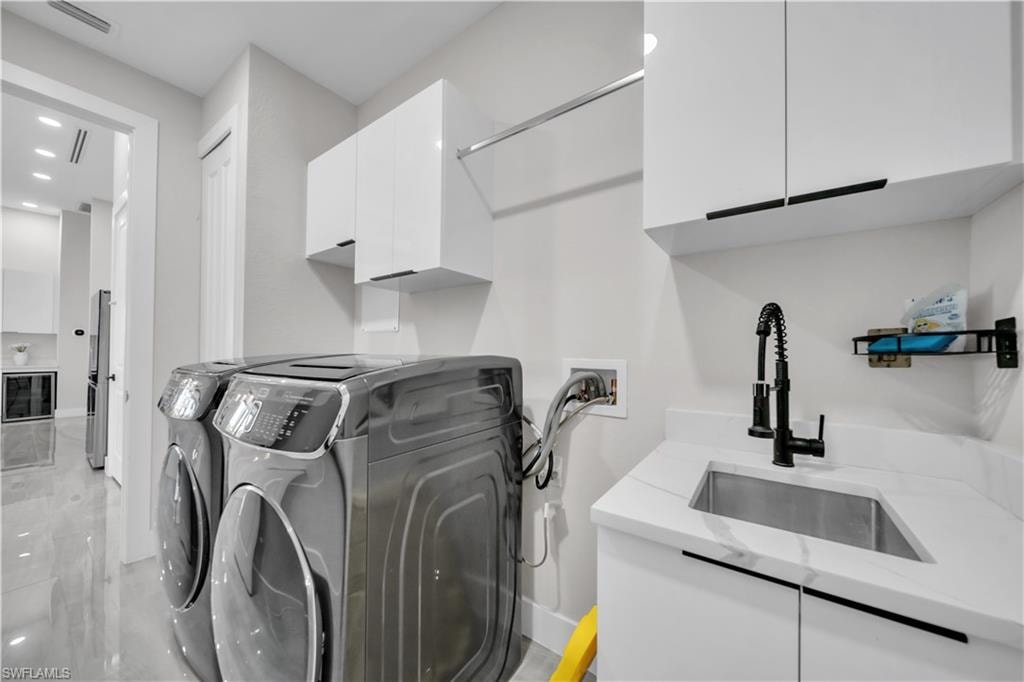 Laundry area featuring a stainless steel sink, white cabinetry with black hardware, and an overhead clothes rack