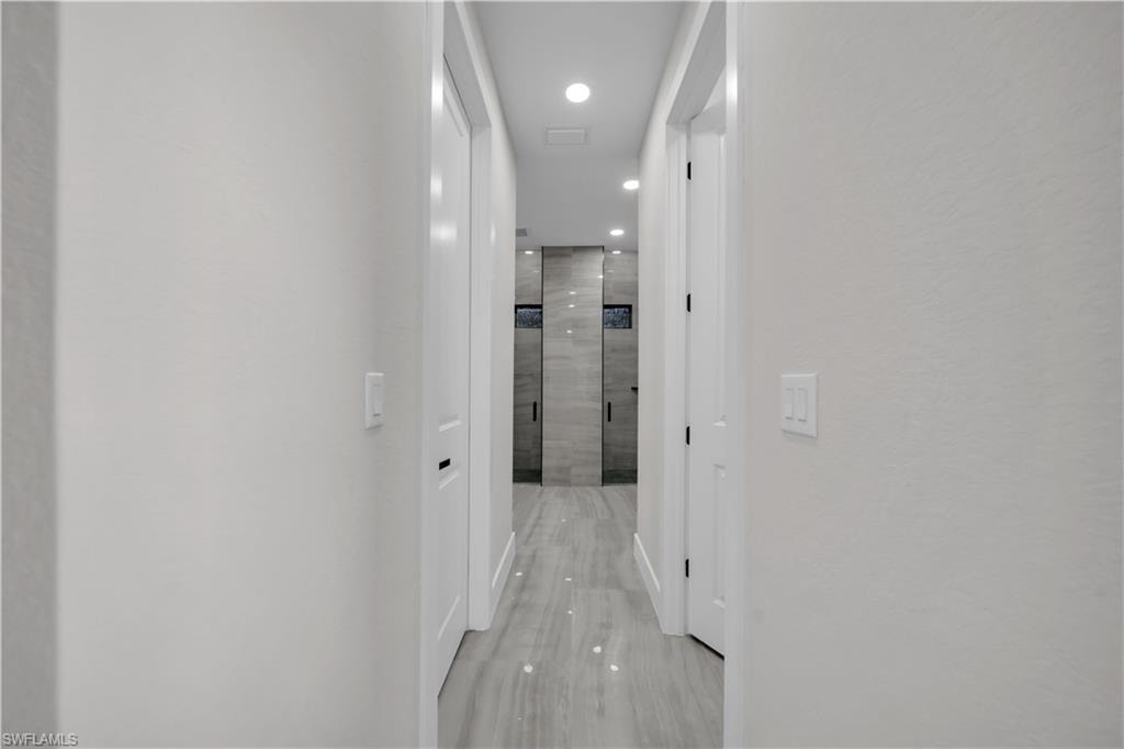 Recessed lighting illuminates a hallway with light-toned walls and wood-finish flooring, leading to a bathroom featuring dual walk-in showers with tile surrounds and built-in niches