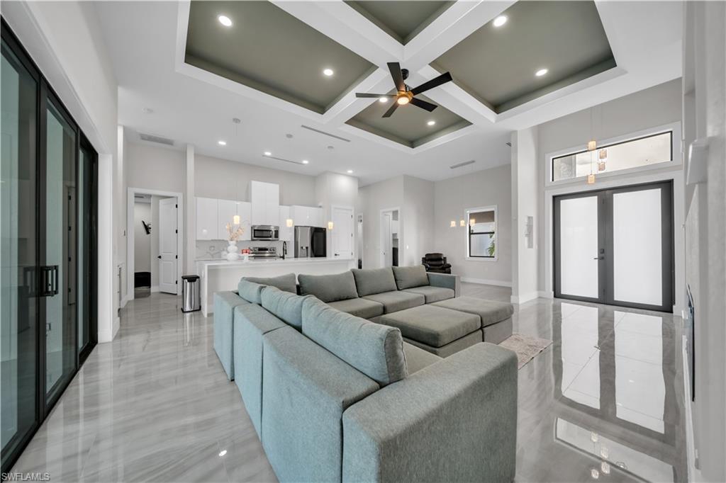 Coffered ceiling with recessed lighting, large format tile flooring, sliding glass doors, white shaker cabinetry, and a kitchen island with pendant lighting