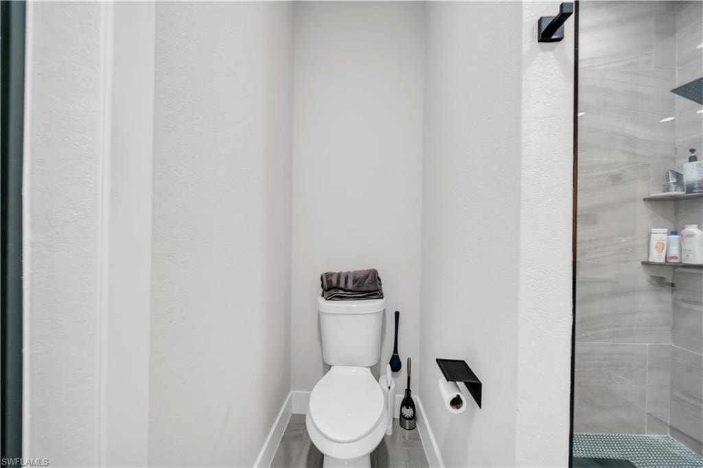Recessed toilet area with wood-finish flooring, featuring a glass-enclosed shower with tiled walls, and built-in shelving