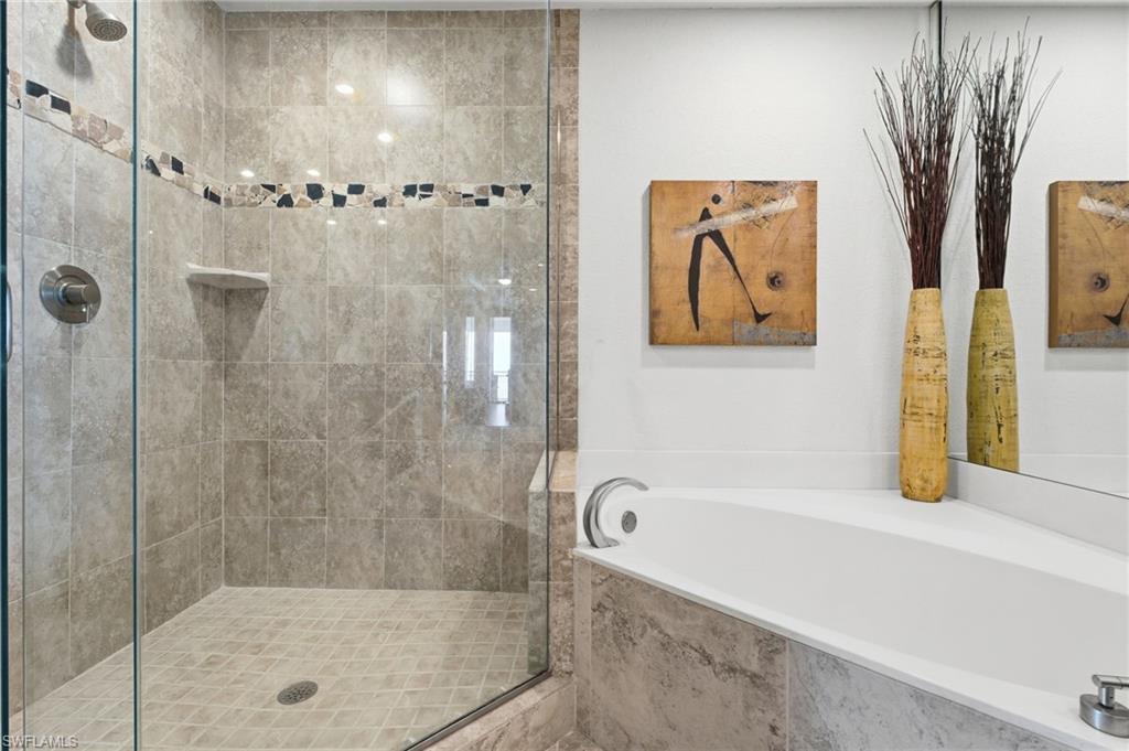 The primary bath offers a spa-like experience with a beautifully appointed walk-in shower featuring a seamless glass enclosure, floor-to-ceiling porcelain tile, and an exquisite decorative listello detail that adds a touch of refined elegance and timeless sophistication.