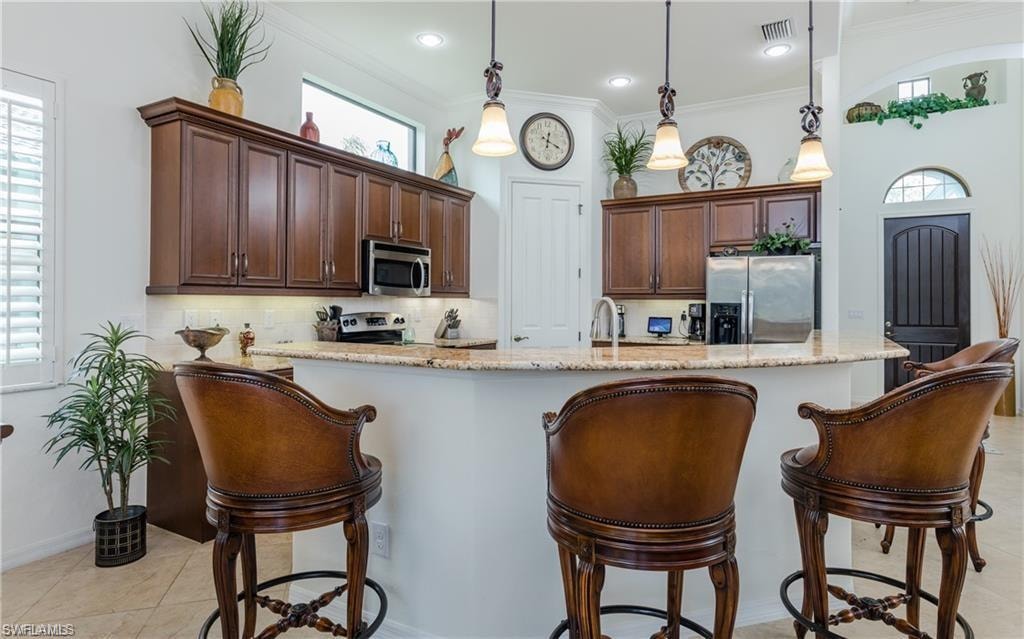 Kitchen with dark brown cabinets, a kitchen breakfast bar, light stone counters, appliances with stainless steel finishes, and hanging light fixtures