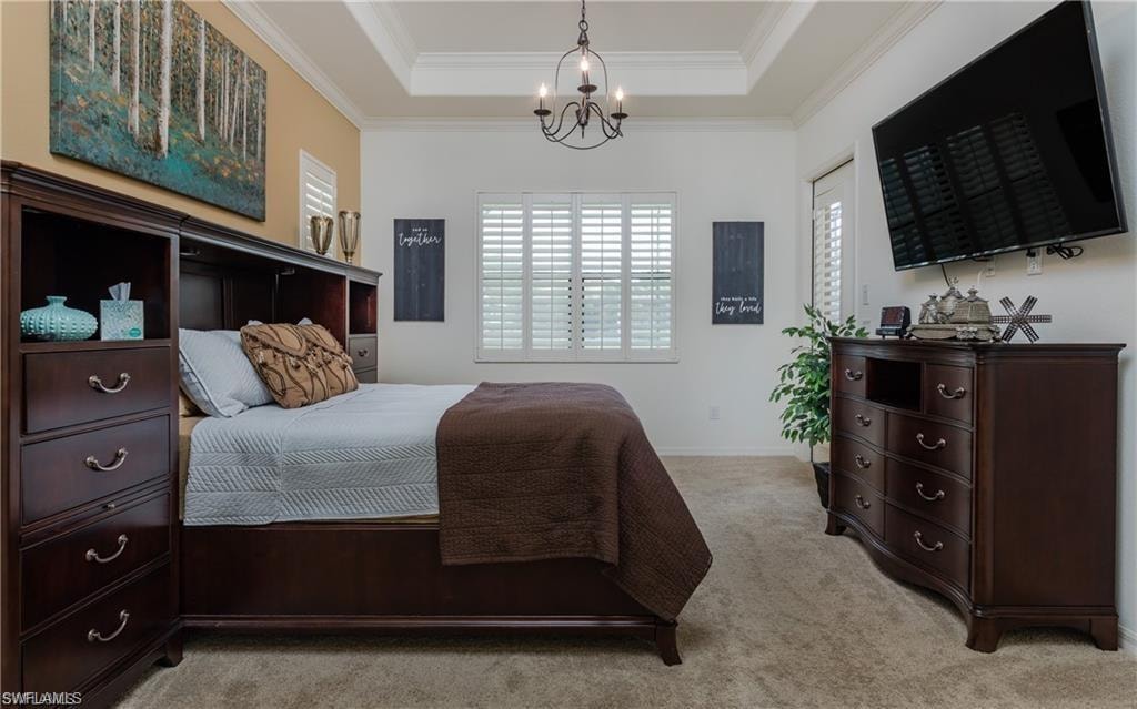 Carpeted bedroom with ornamental molding, a tray ceiling, and a chandelier