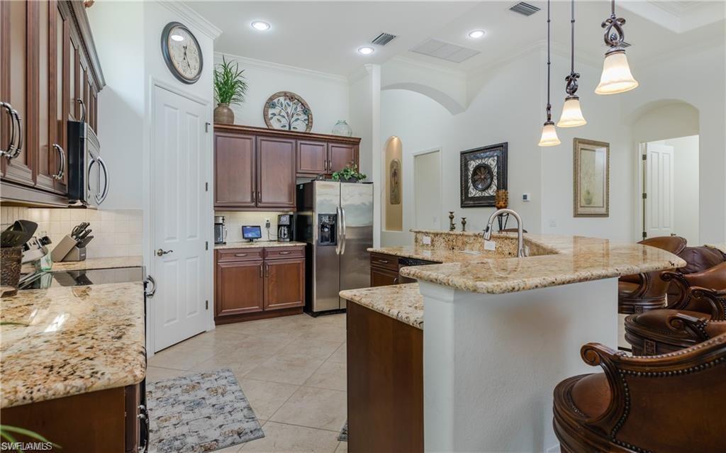 Kitchen with crown molding, decorative light fixtures, an island with sink, arched walkways, and stainless steel appliances