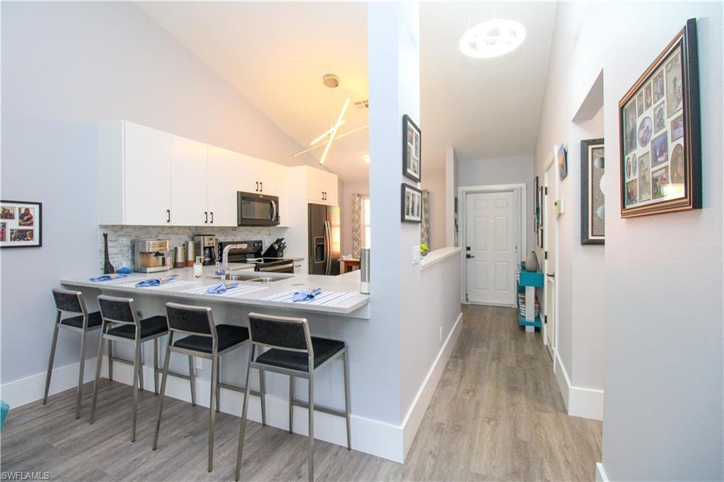 Kitchen with white cabinetry, light hardwood / wood-style floors, lofted ceiling, backsplash, and a kitchen bar